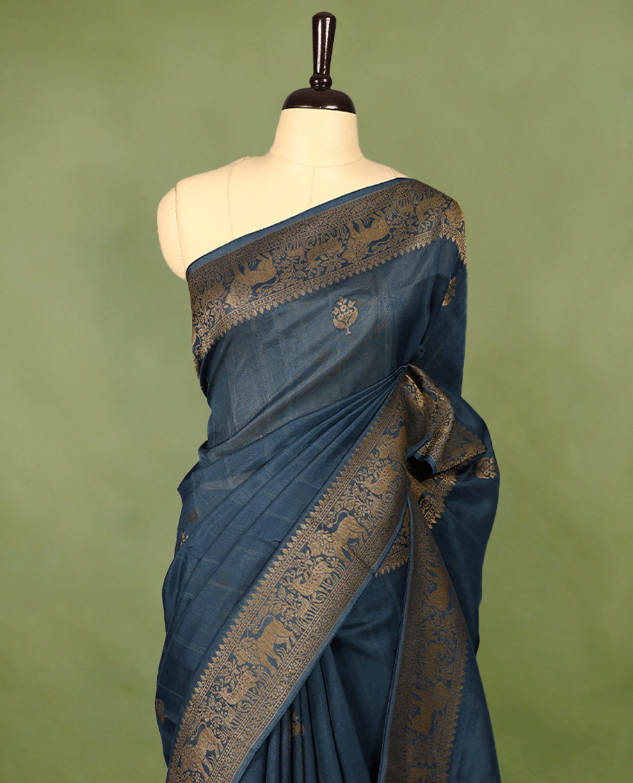 German Blue semi-Banaras tussar georgette saree adorned with antique zari butta motifs on the body, accentuated by a beautifully crafted jungle-themed border, and paired with a matching blouse.