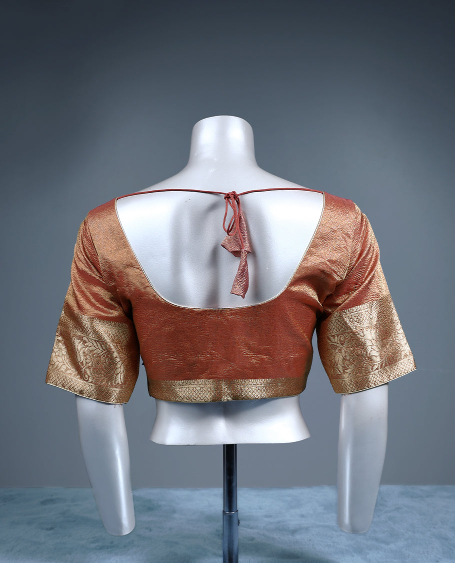 Rust orange colour tissue padded readymade blouse with golden zari weave, complemented by elbow length sleeves featuring intricate floral zari border ideal for traditional silk sarees and festive occasions.