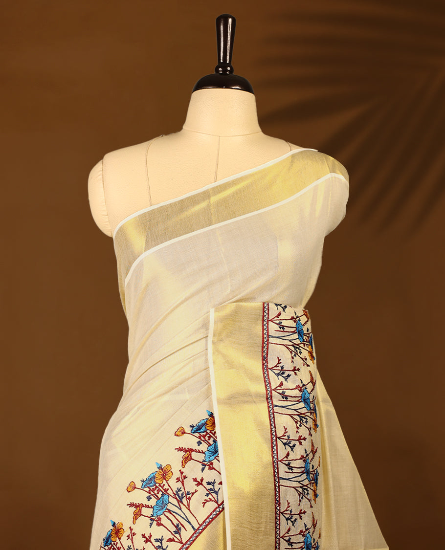 Light Gold colour Tissue Kerala saree featuring Plain body and a beautifully woven Gold Kasavu border with Heavy Blue and mustard colour Floral embroidery work, paired with a matching blouse perfect for festive occasions.