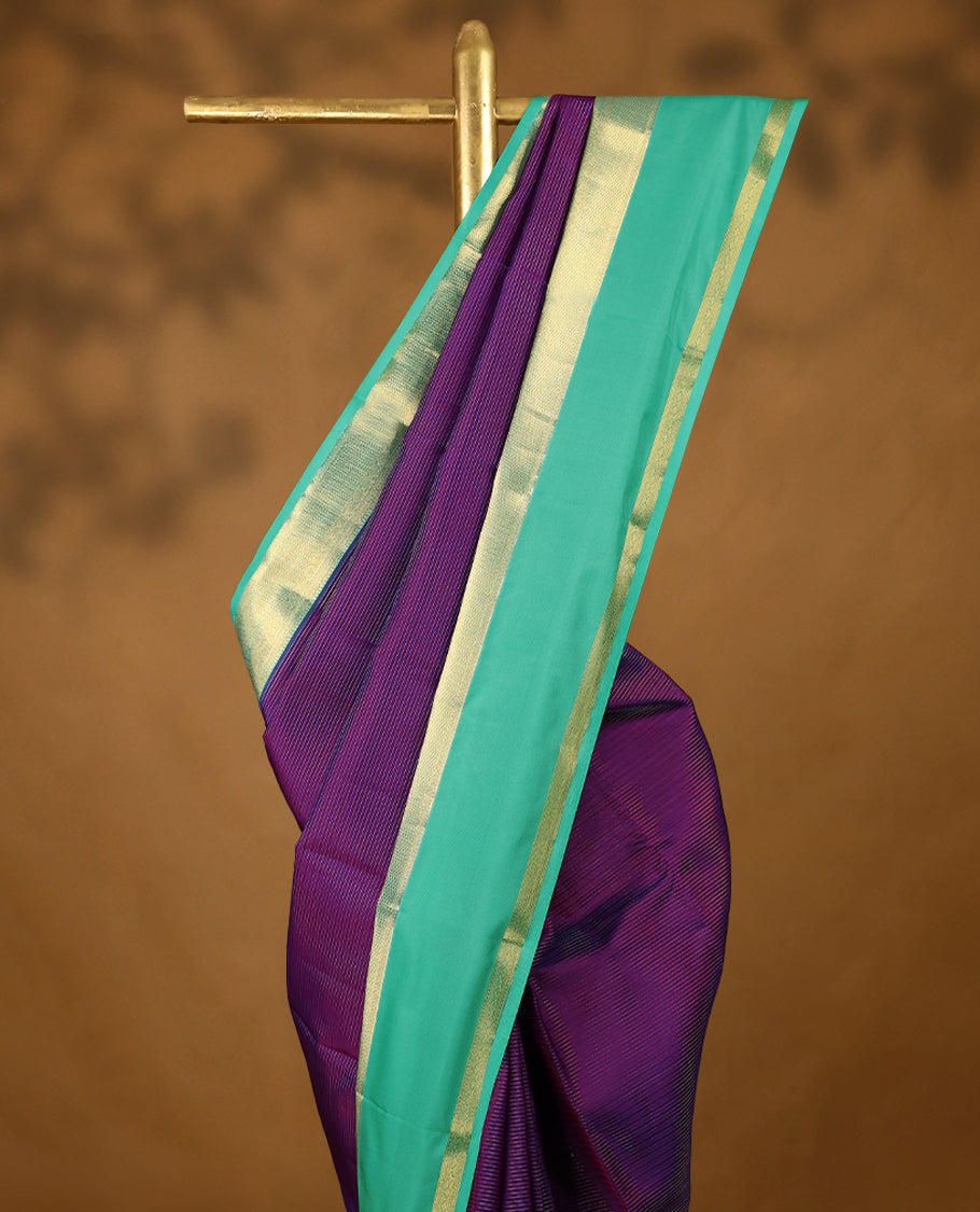 Purple Colour soft silk saree adorned with golden zari stripes on the body, complemented by an aqua colour traditional border and a matching contrast blouse