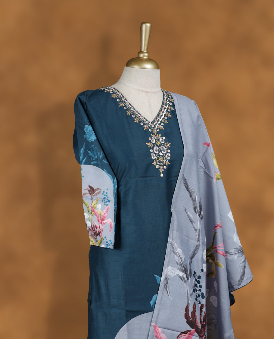 Teal blue colour churidar set featuring V neckline, half sleeves, and embellished floral embroidery on body, paired with a contrasting grey floral printed dupatta.