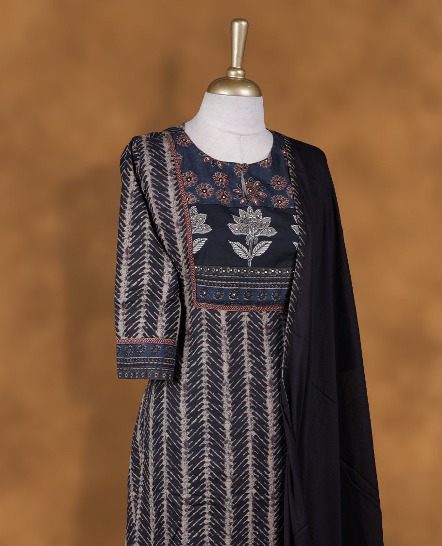 Charcoal black colour churidar set featuring round neckline, three‑fourth sleeves, and ethnic floral printed yoke and body, paired with a solid black dupatta adorned with subtle floral motifs.