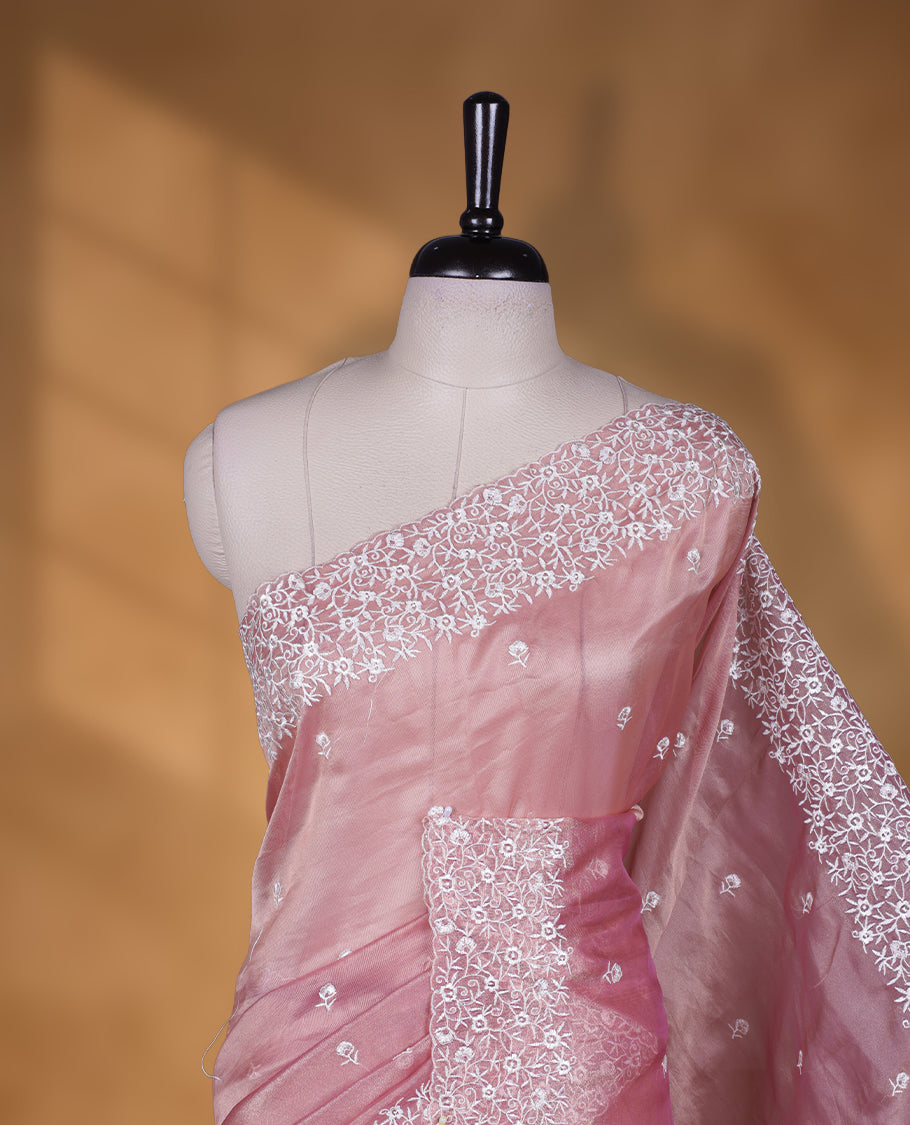 Pink colour net organza designer saree featuring a subtle self patterned body and an intricately scalloped floral thread embroidered border all around, complemented by a coordinating embroidered pallu and paired with a matching blouse.