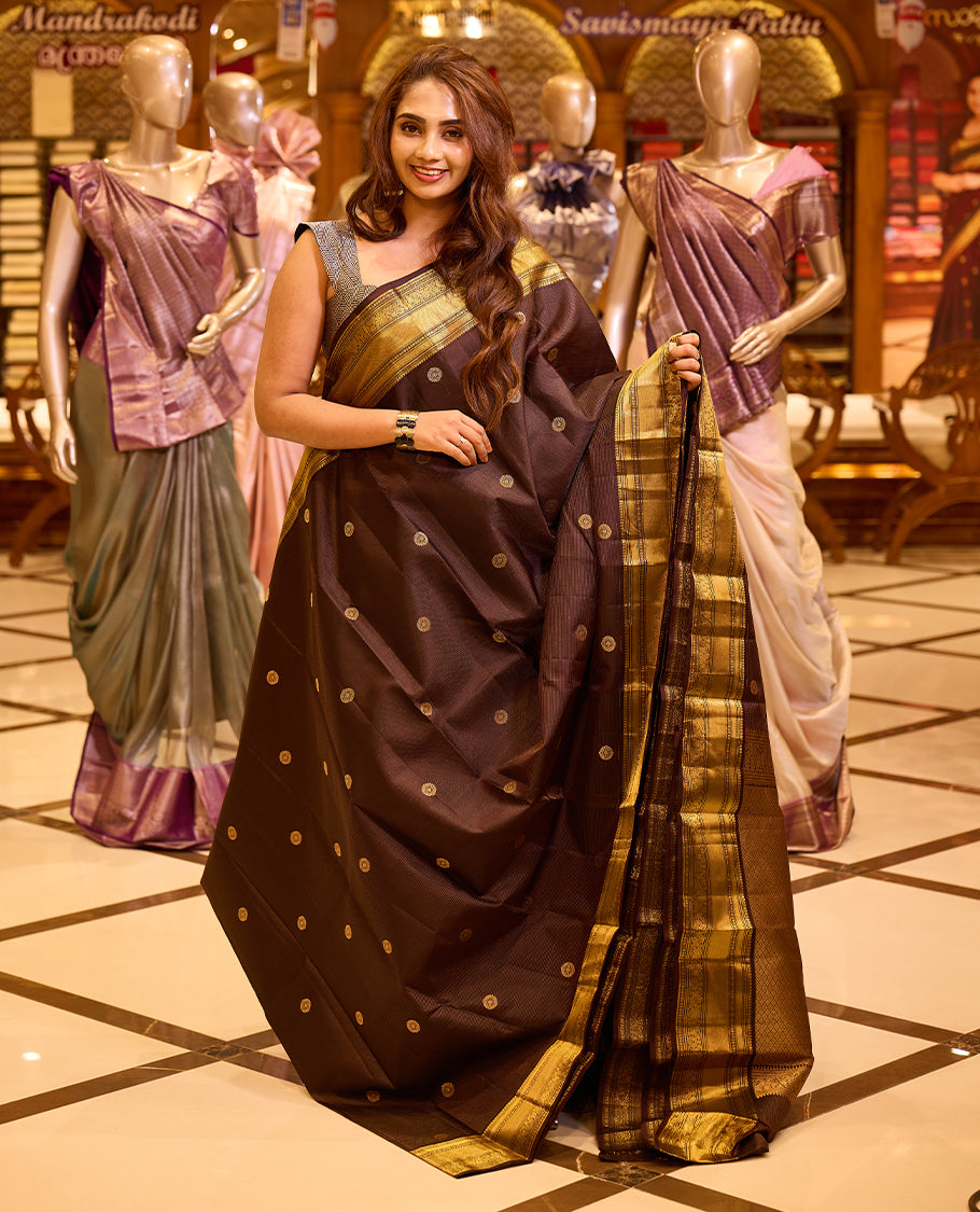 Graceful deep chocolate brown colour Kancheepuram silk saree adorned with delicate gold zari motifs across the body, beautifully finished with a broad traditional gold zari border, exuding timeless elegance and paired with a matching blouse piece