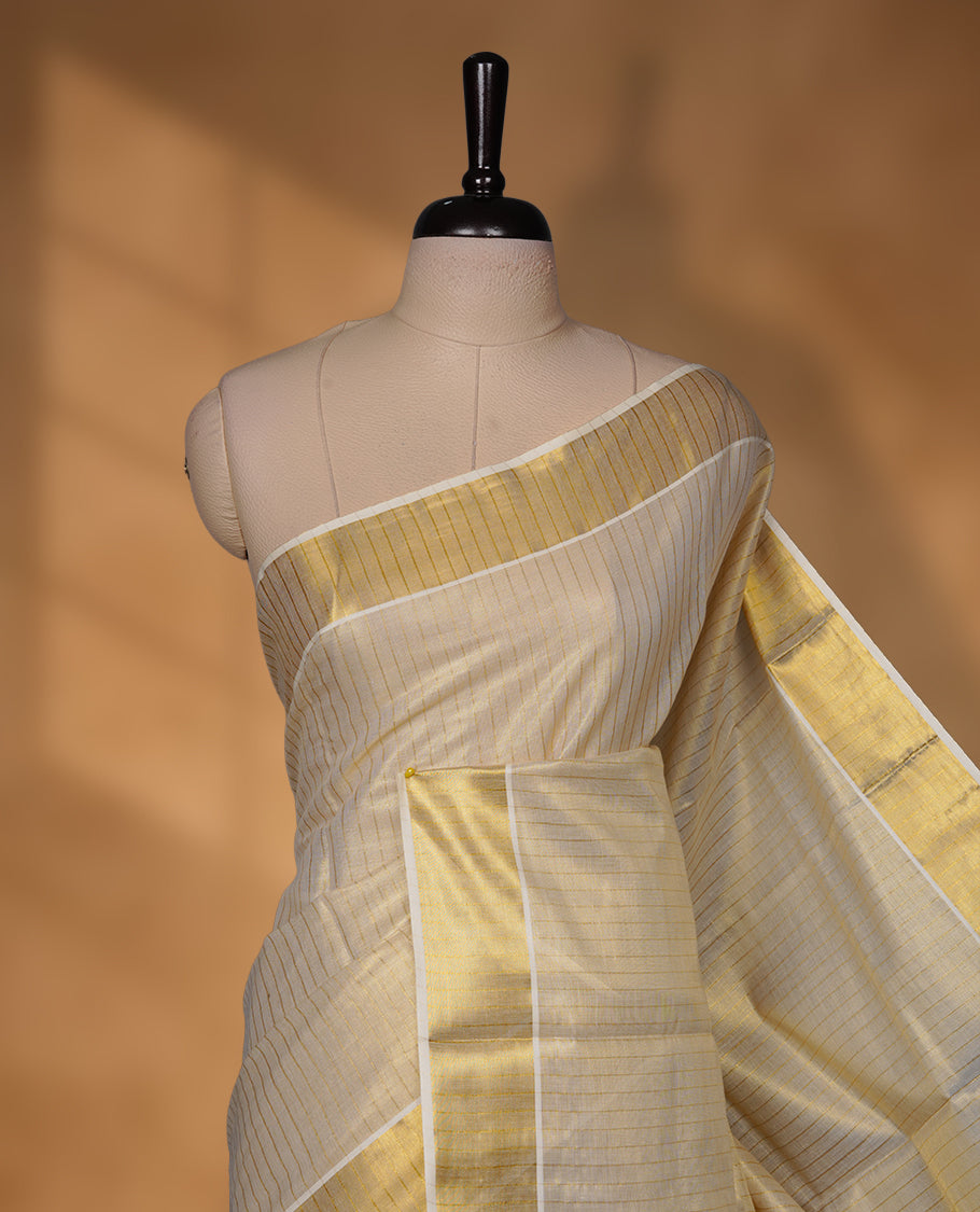 Off-white colour tissue Kerala saree with a timeless gold kasavu border, featuring a subtle striped weave across the body and pallu, paired with a matching blouse.