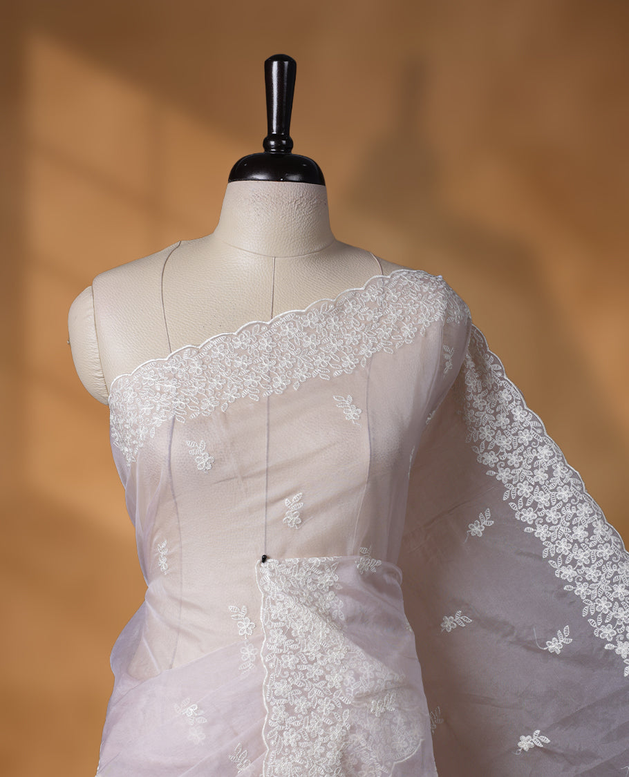 Cream colour organza designer saree featuring a subtle self patterned body and an intricately scalloped floral thread embroidered border all around, complemented by a coordinating embroidered pallu and paired with a matching blouse.