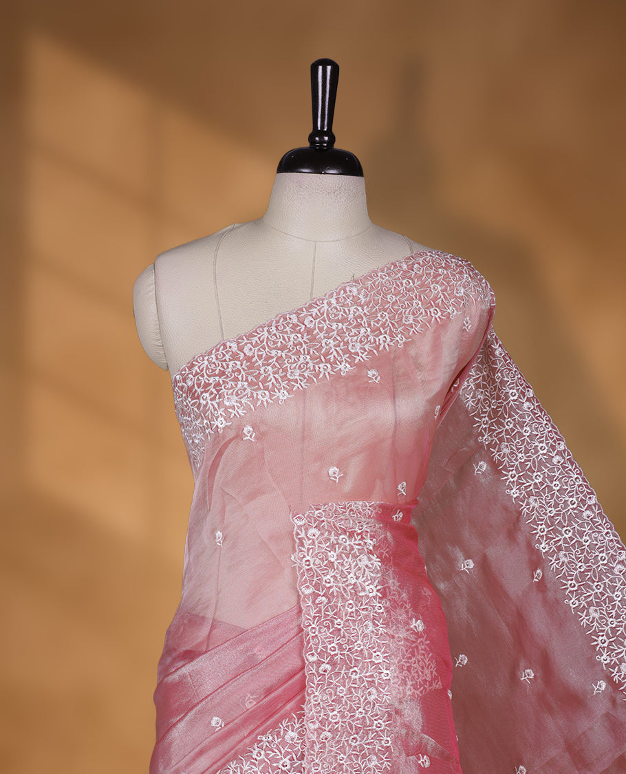 Peach colour net organza designer saree featuring a subtle self patterned body and an intricately scalloped floral thread embroidered border all around, complemented by a coordinating embroidered pallu and paired with a matching blouse.