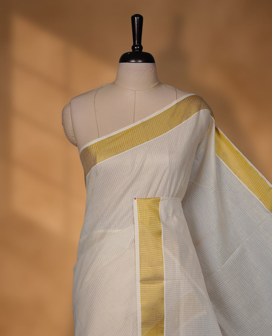 Off-white colour cotton Kerala saree with a subtle self-woven texture, finished with a traditional gold kasavu border across the body and pallu, paired with a matching blouse.