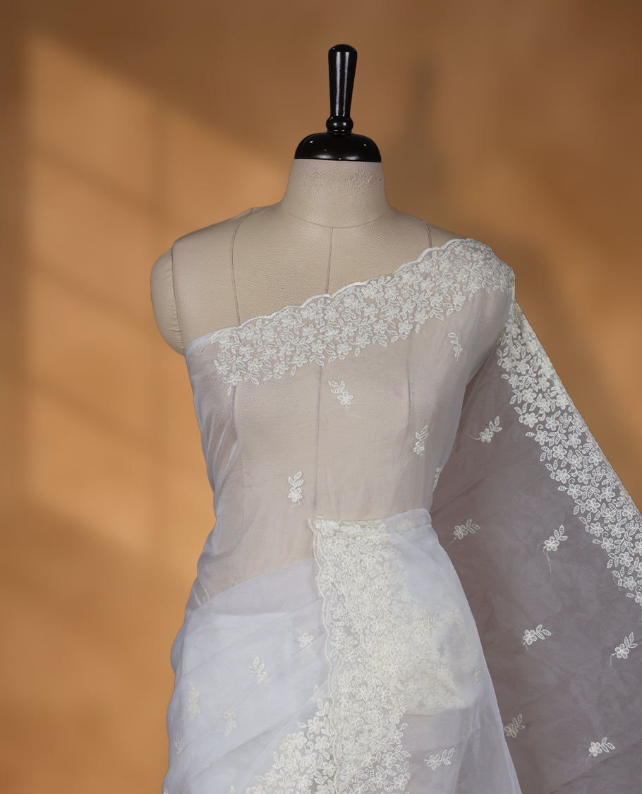 Light yellow colour organza designer saree featuring a subtle self patterned body and an intricately scalloped floral thread embroidered border all around, complemented by a coordinating embroidered pallu and paired with a matching blouse.