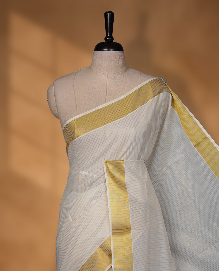 Off-white colour cotton Kerala saree featuring a traditional gold kasavu border with a fine striped texture across the body and pallu, offering a clean, elegant look, and paired with a matching blouse.