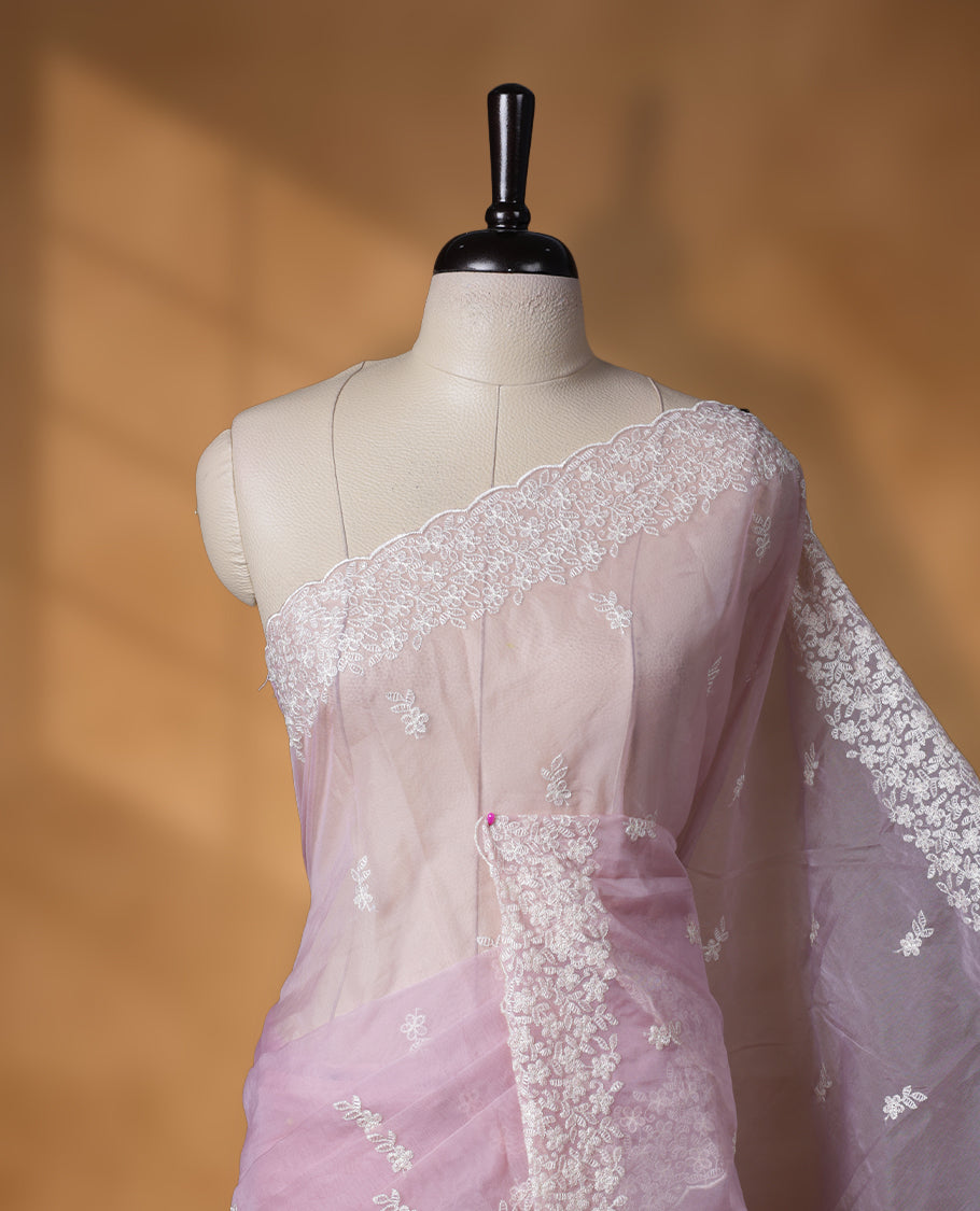 Light Pink colour organza designer saree featuring a subtle self patterned body and an intricately scalloped floral thread embroidered border all around, complemented by a coordinating embroidered pallu and paired with a matching blouse.