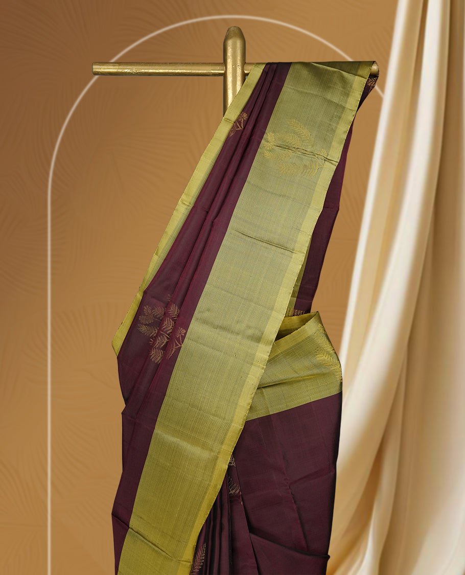 Maroon colour soft silk saree adorned with small golden buttas, enhanced by a shimmering light olive green zari border and pallu with delicate motifs & paired with a matching blouse.