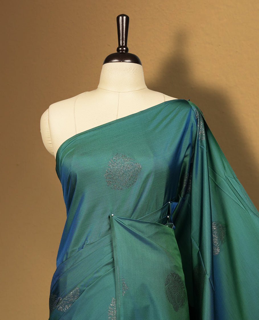 Dual tone blue green semi soft silk saree adorned with woven circular motifs on the body, complemented by a rich contrast plum colour woven pallu with tassel detailing & Comes with a matching blouse piece.