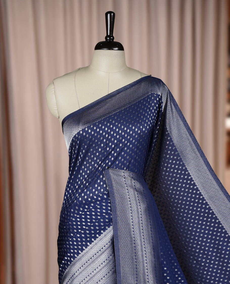 Navy blue colour Banarasi silk saree featuring intricate zari weaving and a soft silk texture, Adorned with silver motifs on the body, complemented by a rich Banarasi border and pallu & Comes with a matching blouse.