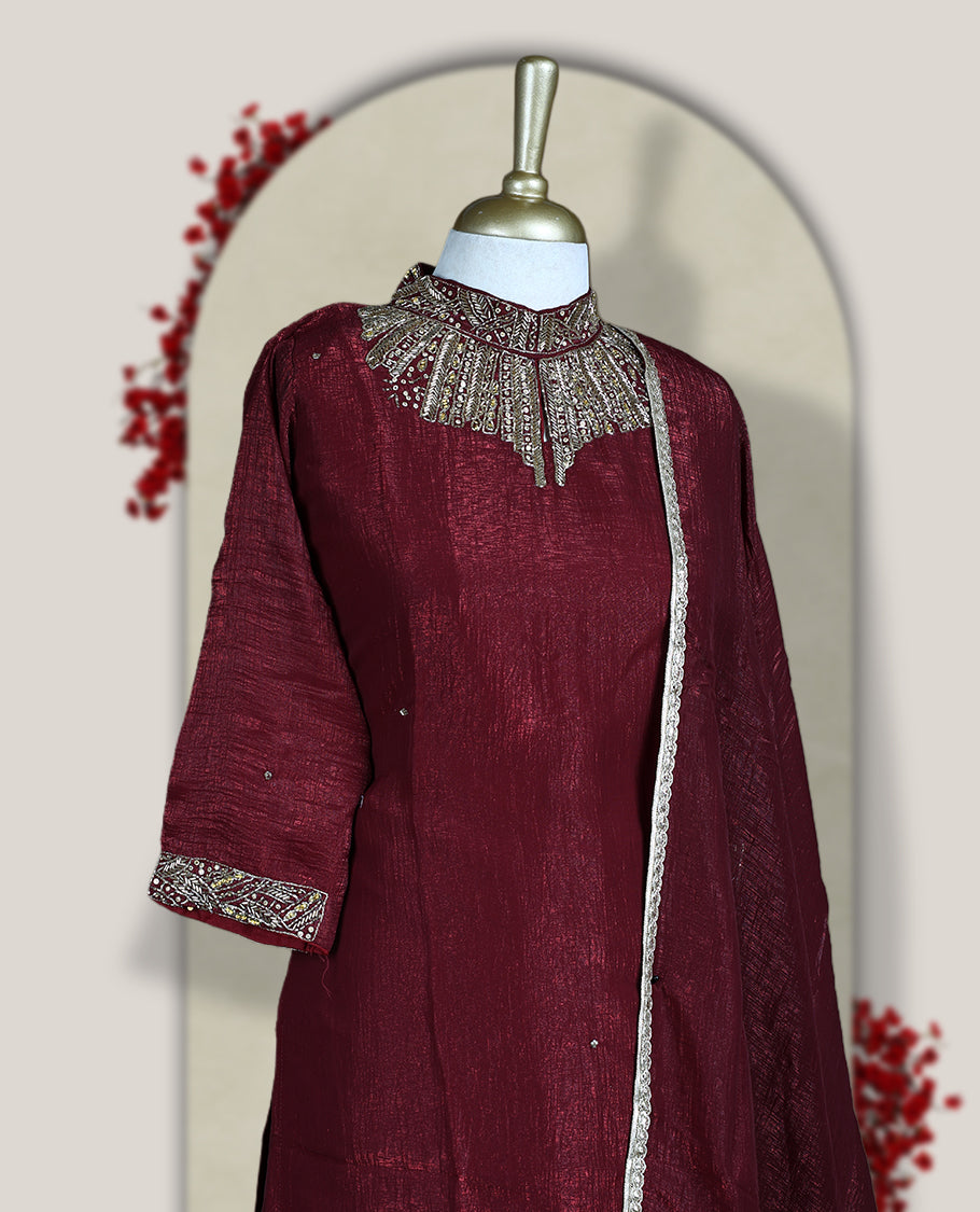 Deep Maroon colour churidar set with a rich sheen, beautifully adorned with golden cut beads work on the neckline and sleeve borders, Paired with a matching dupatta featuring a subtle zari edge, perfect for a regal festive look.