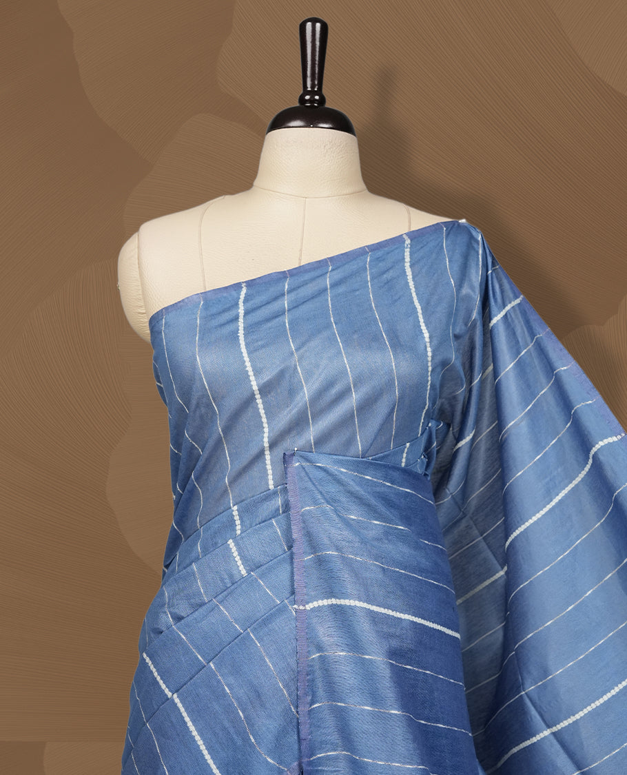 Blue colour semi jute saree with vertical white stripes for a modern appeal, Soft texture, sleek border, tassel pallu, and subtle multicolor detailing & Includes matching blouse piece for a complete look.