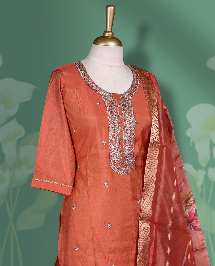 Pinkish Orange colour churidar set featuring elegant gold thread embroidery on the neckline, sleeves, and scattered motifs across the body, Paired with a matching embroidered & floral printed pattern dupatta