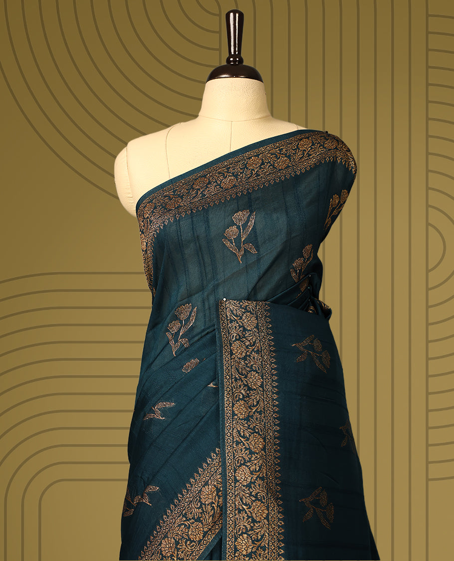 Dark teal green semi Banaras tussar saree adorned with golden floral motifs along the border and scattered designs across the body, finished with a rich golden zari pallu, paired with a matching blouse.