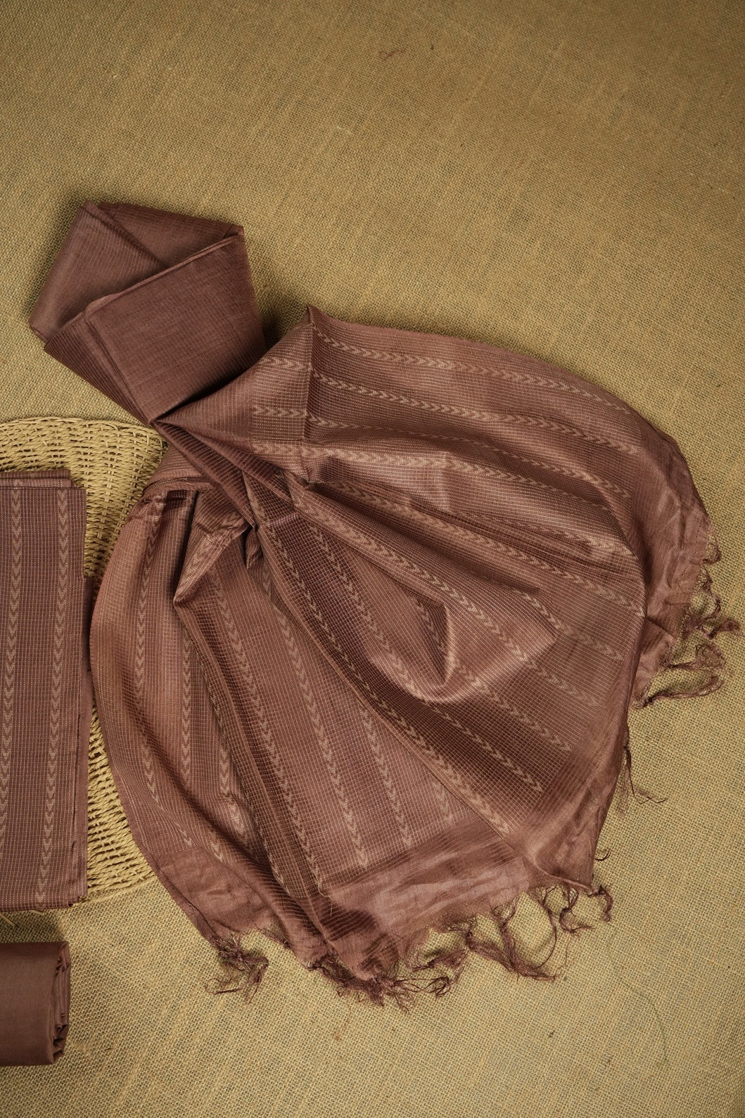 Dusty brown colour tussar suit material adorned with intricate woven patterns and subtle motifs, exuding ethnic elegance & Paired with a beautifully bordered dupatta and a matching plain bottom.