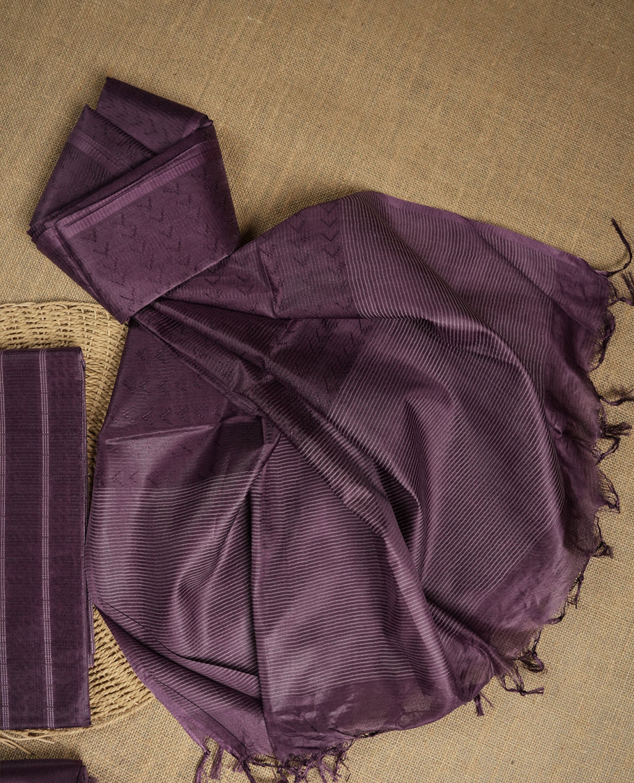 Dark lavender tussar suit material featuring a subtle self woven pattern and vertical lines on the body, paired with a lightweight matching dupatta with tassel edges and a plain bottom piece.
