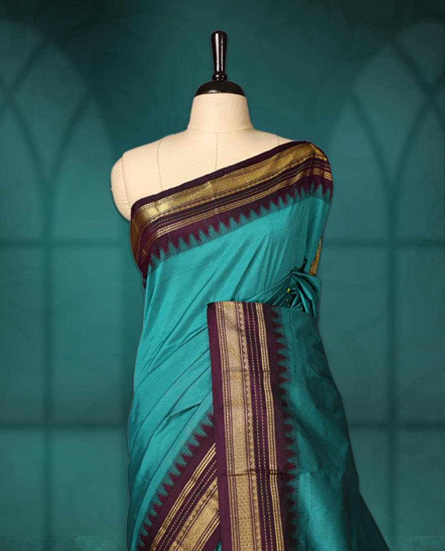 Peacock green semi silk saree with plain body, vibrant deep violet pallu and matching violet border adorned with golden zari, accented with temple motifs along the edges, Paired with a matching blouse, perfect for festive occasions.