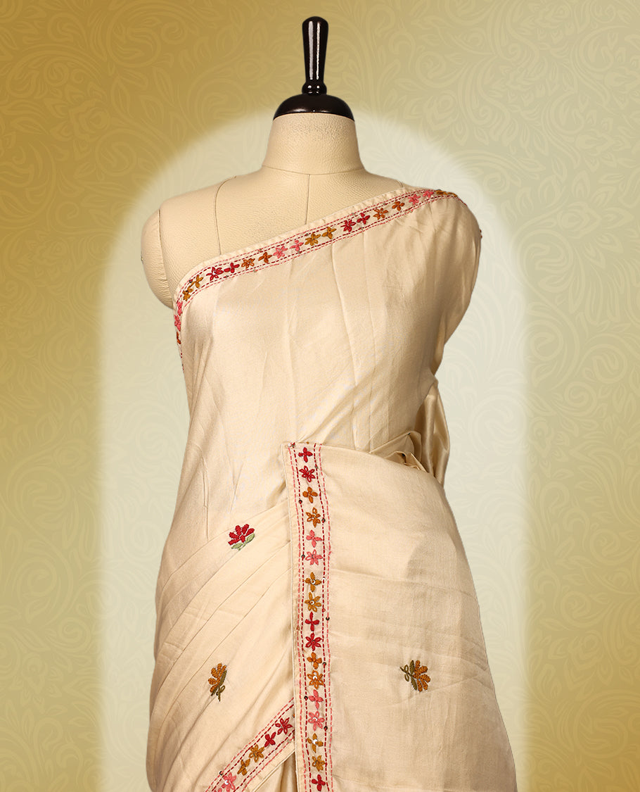 Cream colour pure tussar saree adorned with delicate pink and green floral embroidery along the border and scattered motifs across the body, paired with a matching blouse.