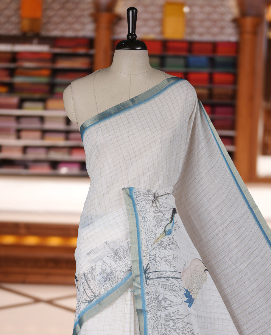 Off white colour Soft cotton saree featuring elegant bird prints along the edges, a stylish checked body, and a beautifully designed blue border & Paired with a matching blouse piece.