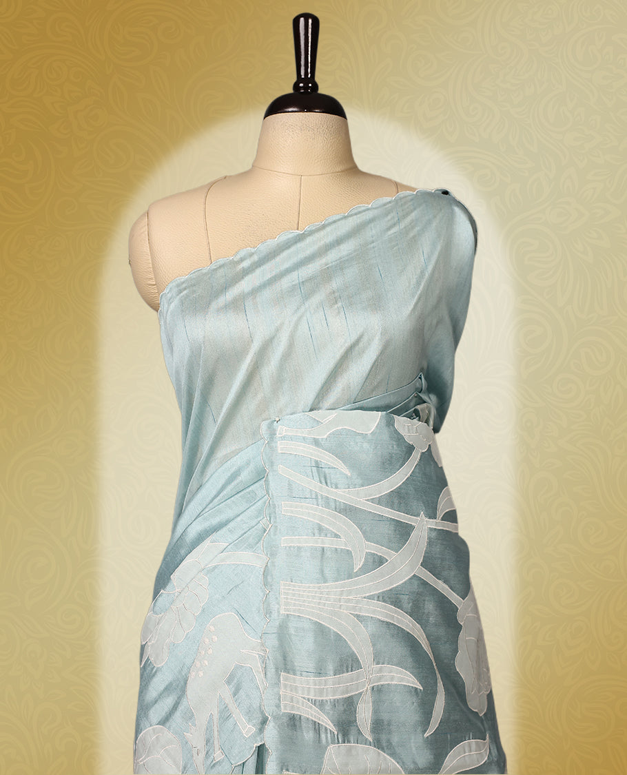 Sky Blue colour semi tussar saree adorned with elegant white applique work in leaf and floral designs across the body and border, paired with a matching blouse.