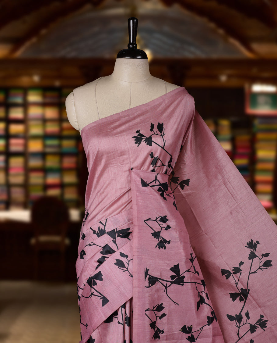 Pastel Pink colour Semi tussar silk saree adorned with black floral prints on the body and an elegant pallu & Comes with a matching blouse piece for a classy look.