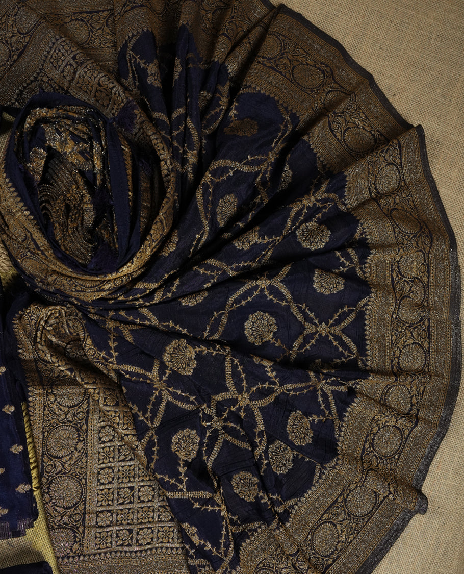 Navy blue colour suit material adorned with intricate golden zari weaving, exuding timeless elegance & Paired with a beautifully woven dupatta featuring floral and geometric motifs and a matching plain bottom.