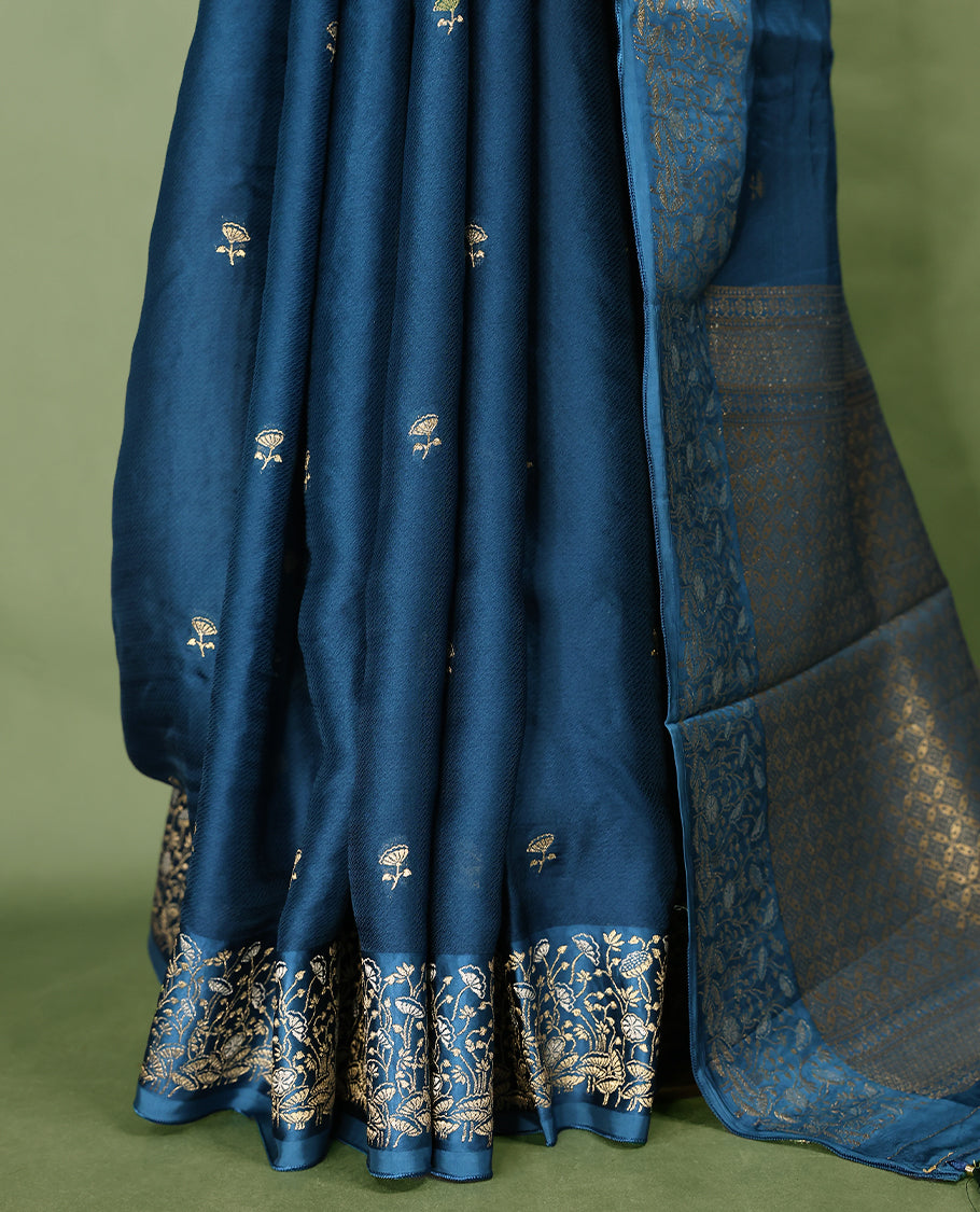 Peacock Blue colour pure Banaras crepe saree showcases elegant Gold zari Flower Motifs all over the body, a traditional gold & Silver zari border, a rich intricately woven pallu, and comes with a matching blouse.