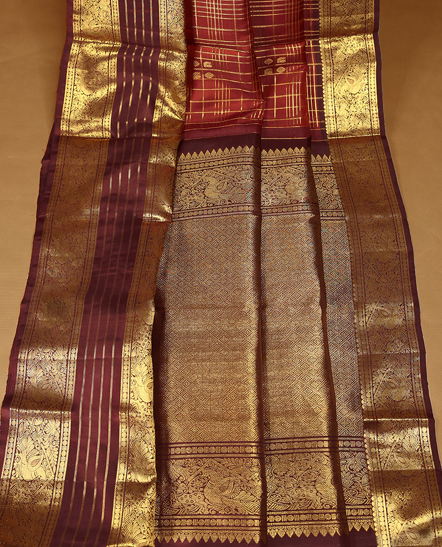 Dark red Colour traditional Kancheepuram silk saree adorned with antique zari check design on the body, featuring a contrasting Traditional border with peacock, deer, and Rudraksham motifs, and paired with a matching blouse.
