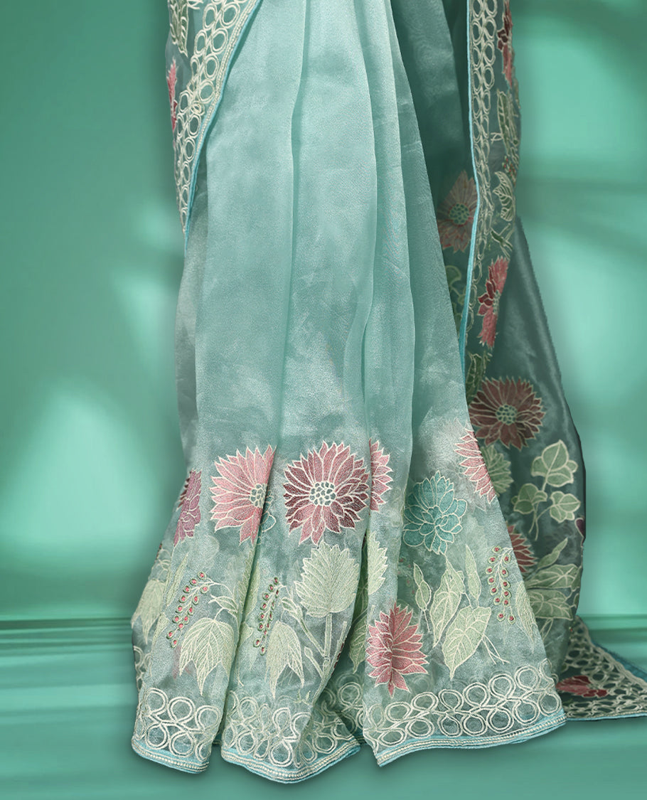 Aqua Blue colour organza designer saree featuring delicate pastel floral embroidery in pink, mint green, and white across the body, with a scalloped border accentuated by floral threadwork, and a gracefully embroidered pallu paired with matching blouse.