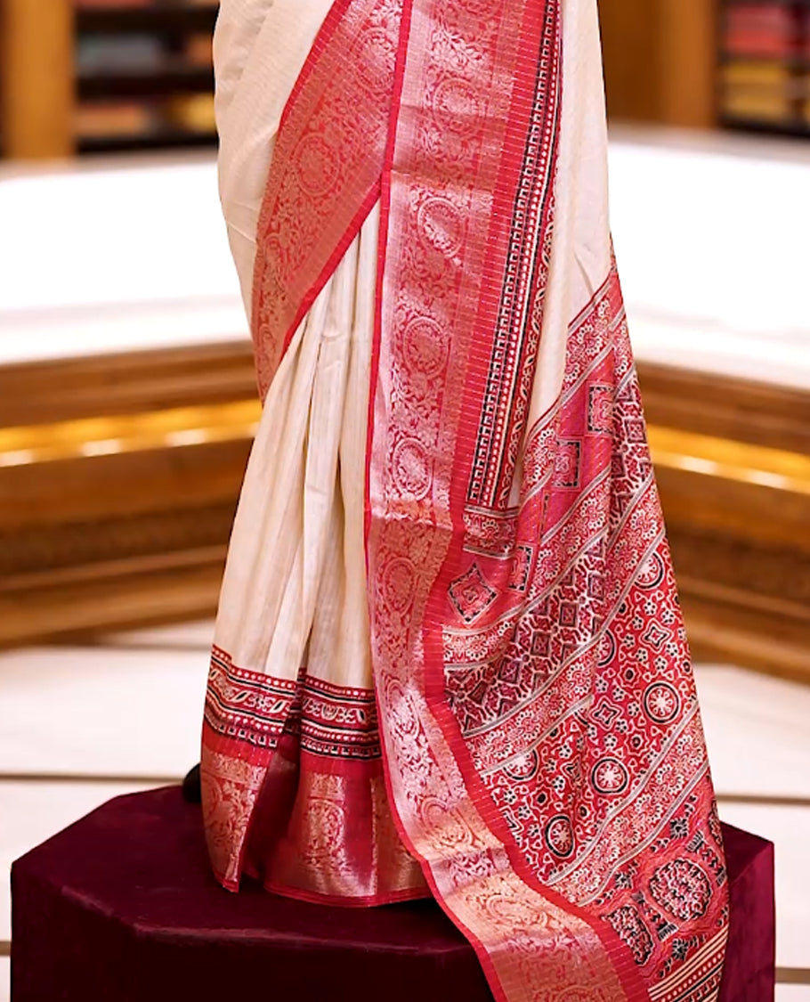 Beige Dolla silk saree featuring antique zari stripes across the body, adorned with a striking Ajrak and Traditional red colour border, ajrak printed pallu and paired with a perfectly matching blouse.
