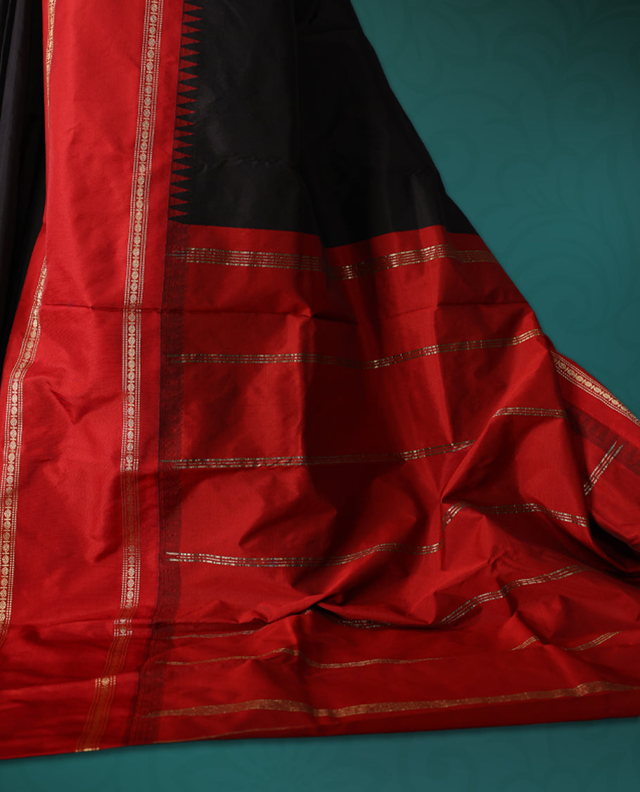 Black semi silk saree with plain body, vibrant red pallu and rich red border adorned with golden zari, accented with temple motifs along the edges, Paired with a matching blouse, perfect for festive occasions.