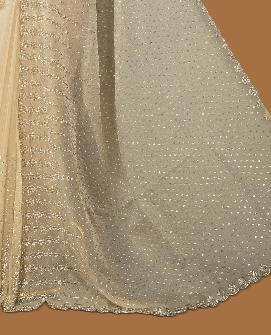 Beige colour net shimmer fancy saree adorned with gold stone buttas all over the body, paired with a delicate stone worked border, with matching blouse