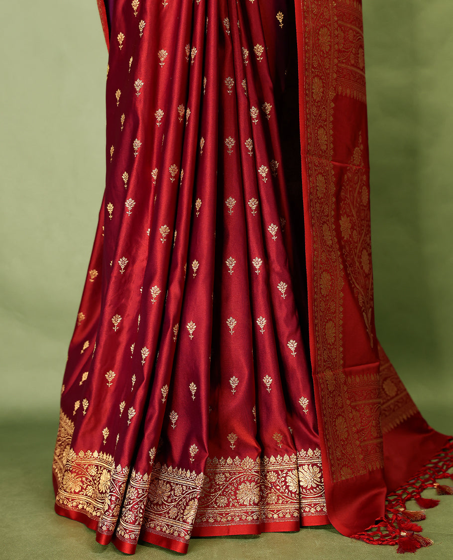 Deep red colour semi Banaras satin crepe saree featuring gold zari woven flower motifs across the body, complemented by an intricately designed traditional banarasi border and richly woven pallu, paired with a matching blouse piece.