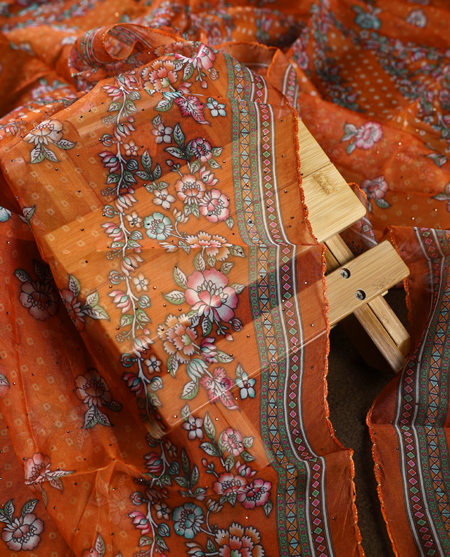 Vibrant orange churidhar material enhanced with delicate floral,stone and vine prints, paired with a plain matching bottom and a beautifully printed dupatta, perfect for festive elegance and traditional charm.