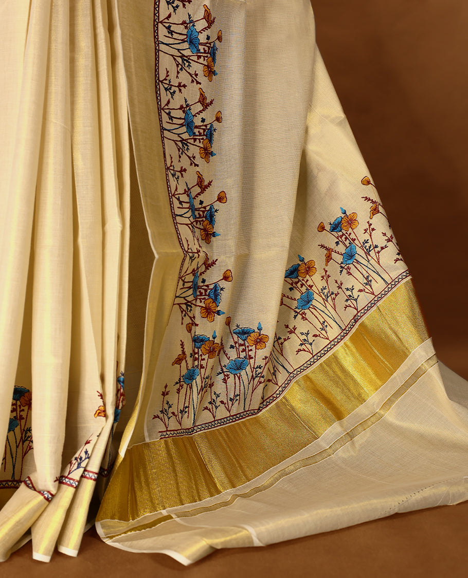 Light Gold colour Tissue Kerala saree featuring Plain body and a beautifully woven Gold Kasavu border with Heavy Blue and mustard colour Floral embroidery work, paired with a matching blouse perfect for festive occasions.