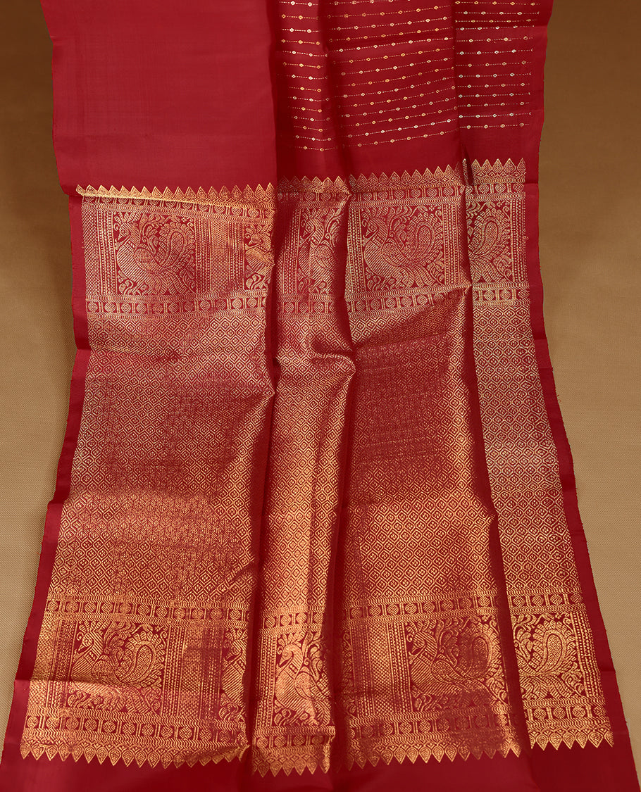 Deep red colour traditional Kancheepuram silk saree adorned with vertical rows of small golden motifs on the body, featuring a self-coloured simple border with floral chakra motifs, and paired with a matching blouse.