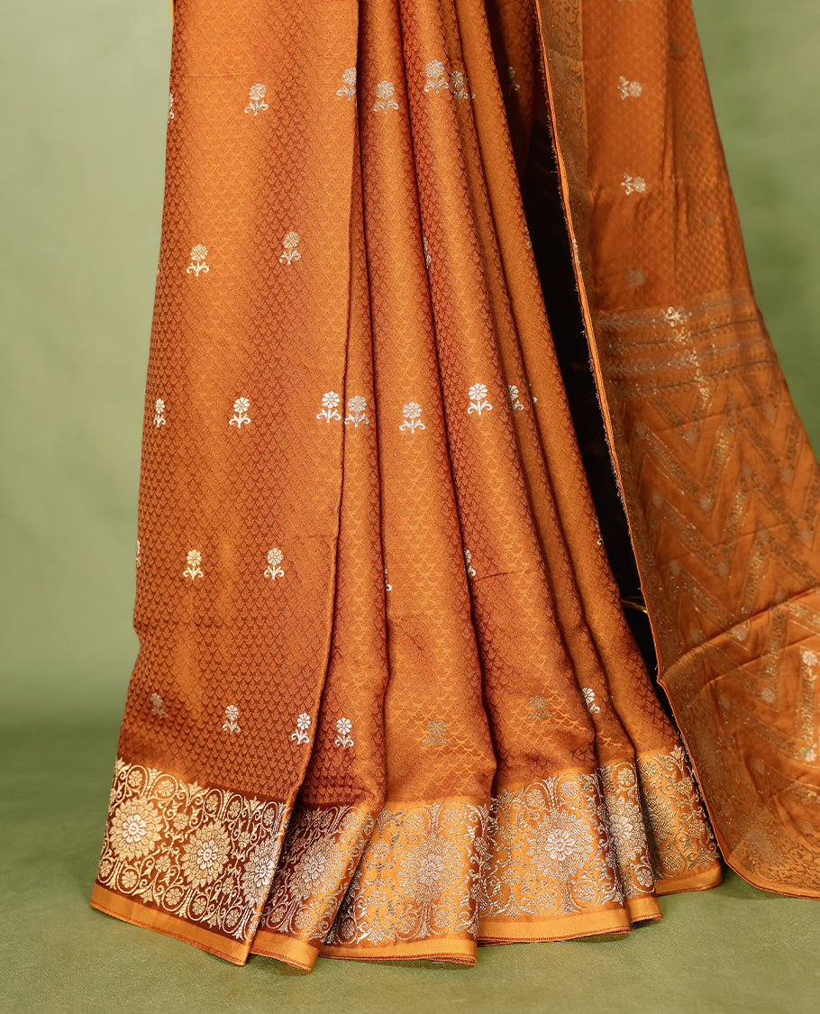 Burnt orange colour pure Banaras crepe saree showcases elegant silver zari Flower Motifs all over the body, a traditional Banarasi gold zari border, a rich intricately woven pallu, and comes with a matching blouse.