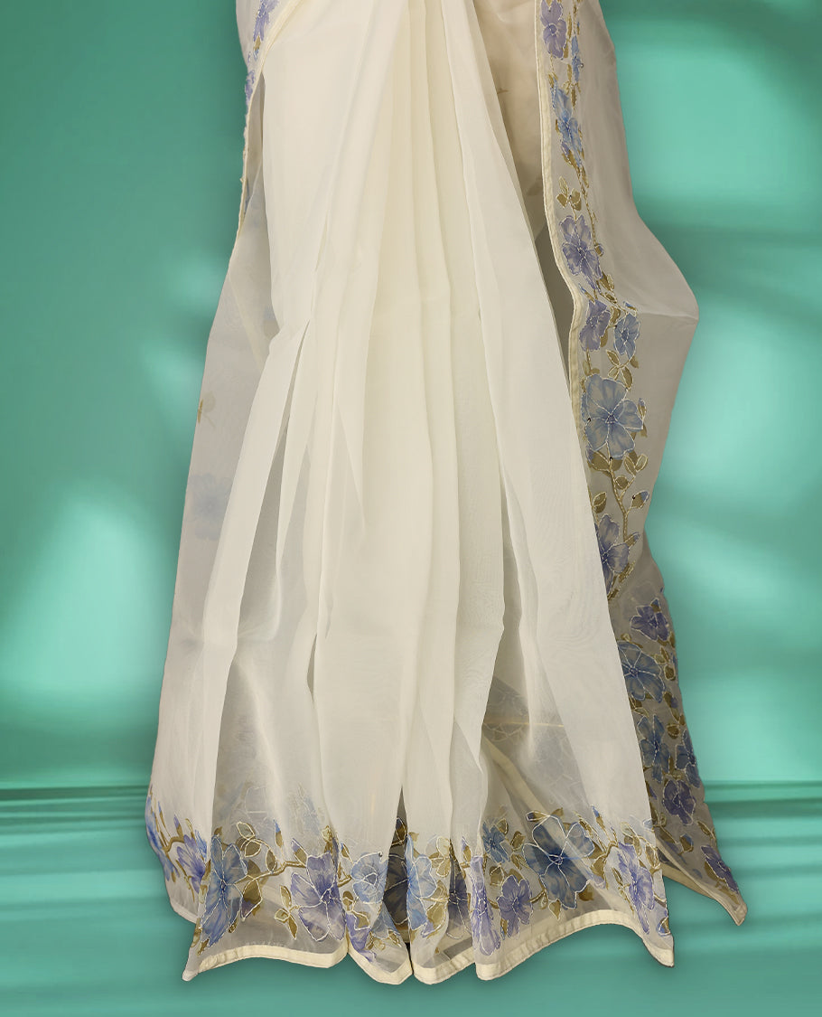 Ivory white colour organza saree adorned with blue floral print with thread detailing on the border and pallu, in a sheer finish that adds elegance, paired with a matching blouse for a graceful look.