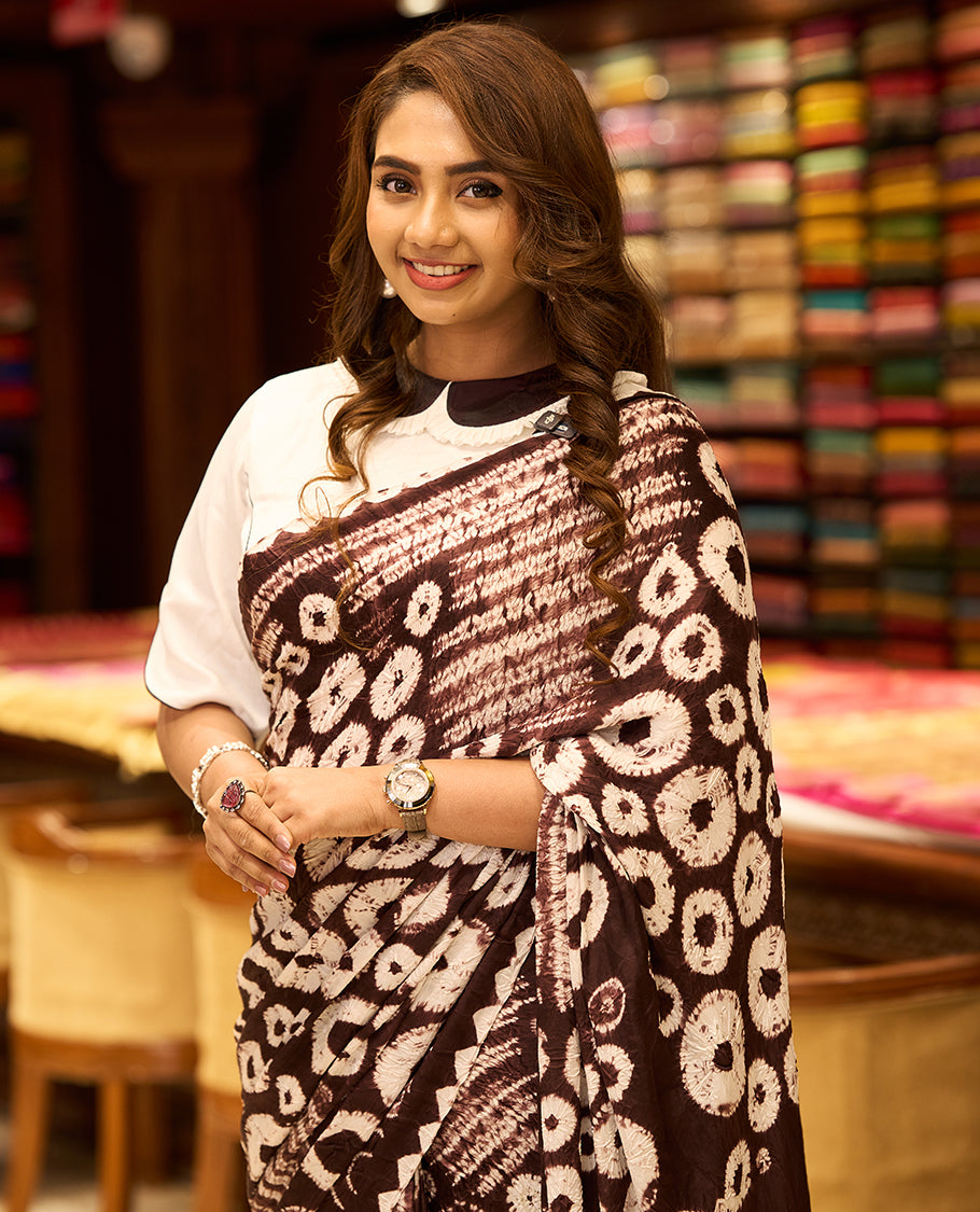 Medium coffee brown colour modal satin crepe saree featuring intricate hand done Shibori and Bandhej designs, enhanced by its smooth texture and paired with a matching blouse.