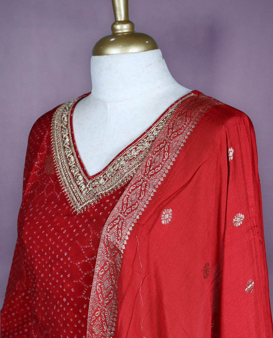 Deep red colour salwar set with V neck and elbow sleeves featuring bandhani inspired dotted pattern with gold motifs paired with matching bottom and dupatta with tassel detail
