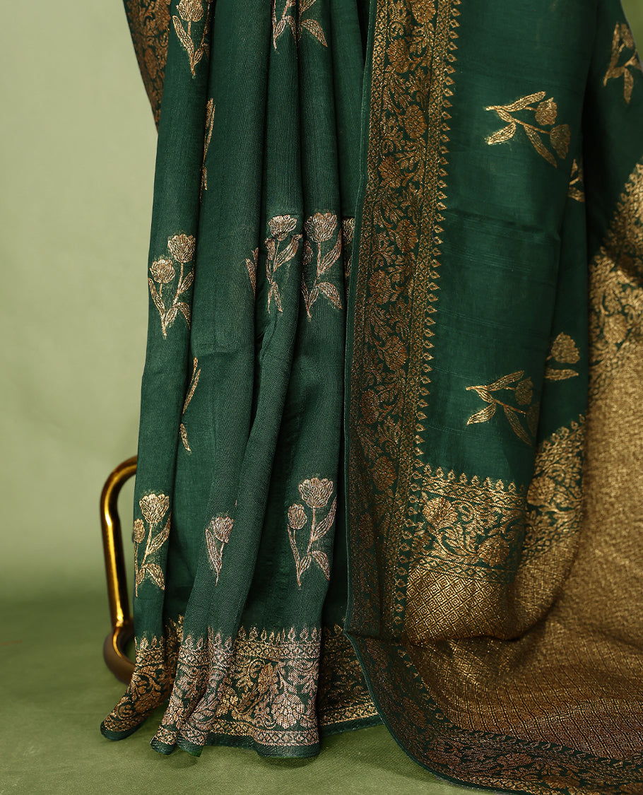 Dark Green colour semi Banaras tussar georgette saree embellished with antique zari flower motifs across the body, complemented by a rich Banaras border and paired with a matching blouse.