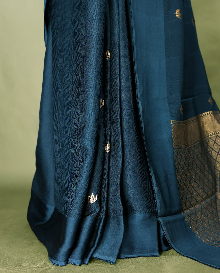Deep teal colour crepe Banaras saree featuring small zari Floral Motifs across the body, without border, a sleek texture, and a rich golden zari pallu with geometric patterns, paired with a matching blouse for a graceful festive look