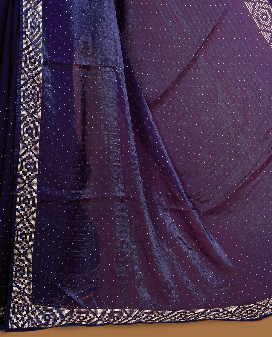 Dark purple colour chiffon designer saree, featuring delicate scattered stone detailing all over the body, highlighted with intricate stone work and a heavy geometric stone pattern along the border and pallu, paired with a matching embellished blouse.