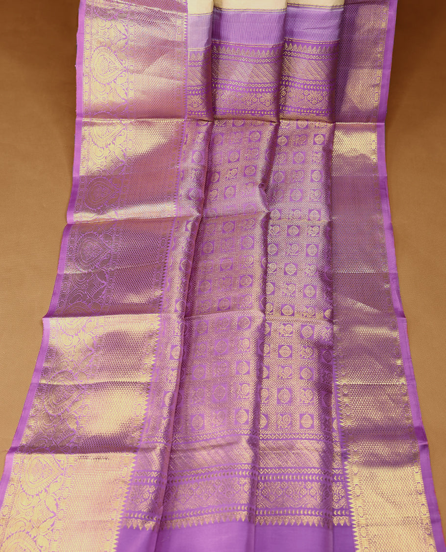 Cream Colour traditional Kancheepuram silk saree adorned with golden motifs on the body, featuring a Light Purple traditional border with Rudraksham and mango designs, paired with a matching blouse.