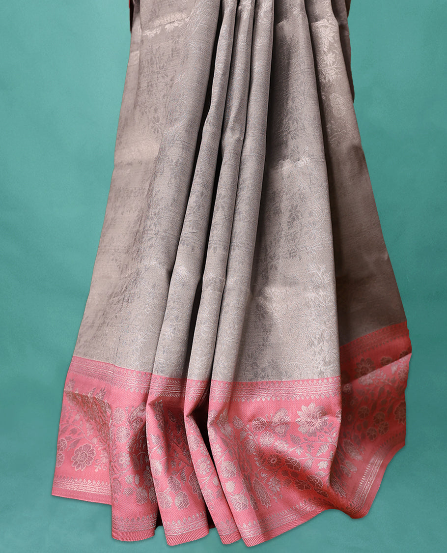 Silver coloured semi silk saree featuring a self coloured floral jaal design on the body, paired with an onion coloured border and matching blouse.