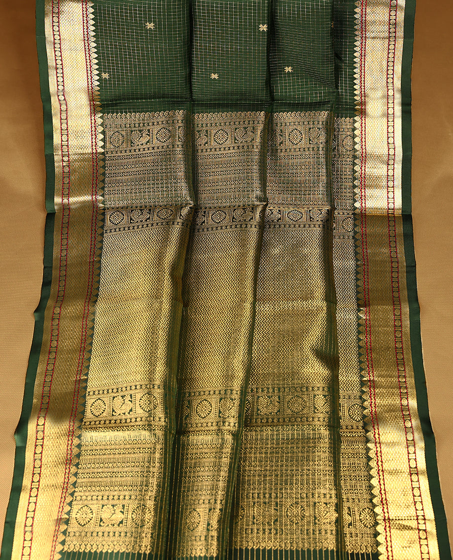 Dark green Colour traditional Kancheepuram silk saree adorned with an antique zari grid pattern and small golden Floral motifs on the body, featuring a border with paisley and Rudraksham motifs, and paired with a matching blouse.